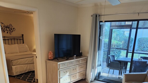 A spacious living area with a large TV, a dining table, and a balcony with a view. - Gulf Gate - Quaint and fresh 1st floor condo w/covered parking (Sarasota)