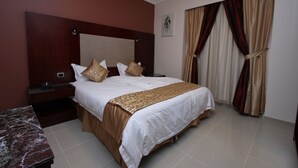 A hotel room with a large bed, a nightstand, a marble table, and a window with curtains.