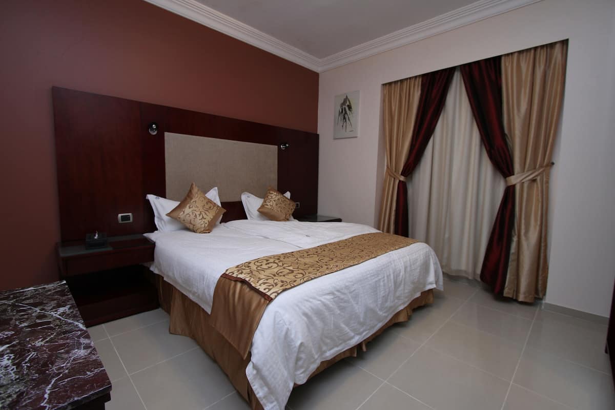 A hotel room with a large bed, a nightstand, a marble table, and a window with curtains.