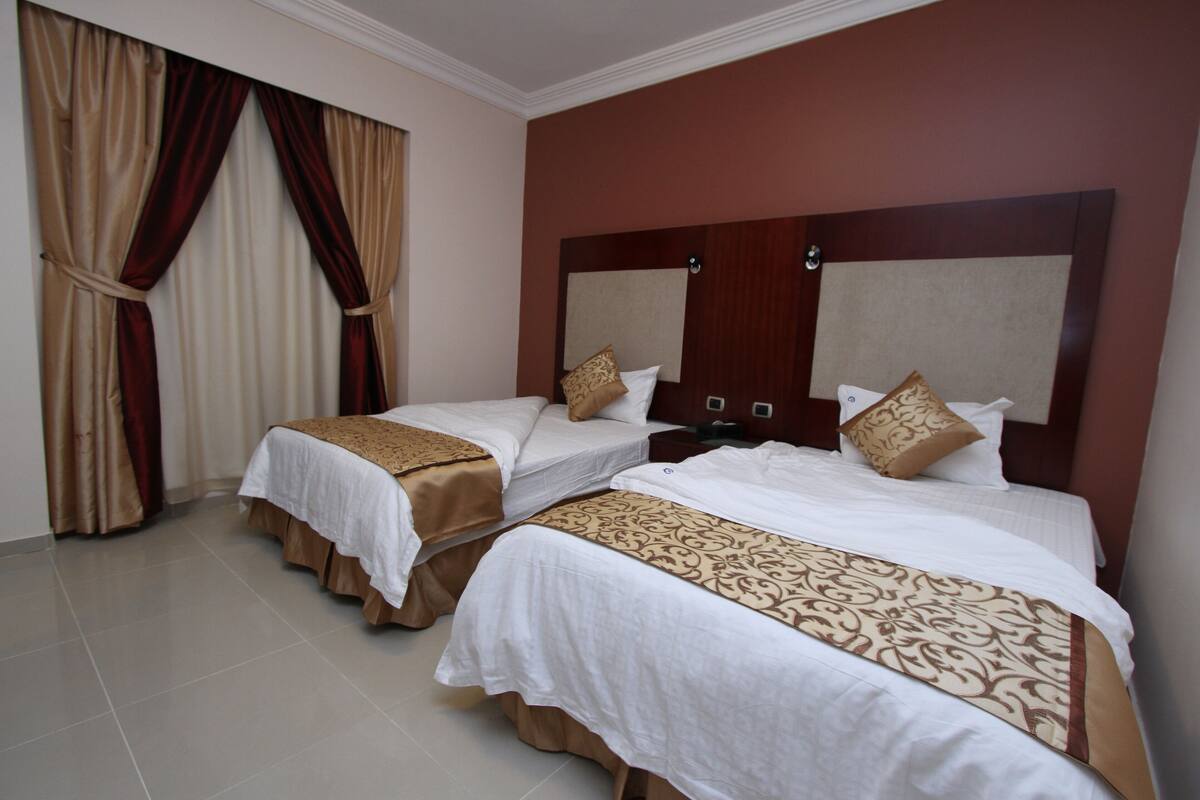 A hotel room with two beds, beige curtains, and a wooden headboard.