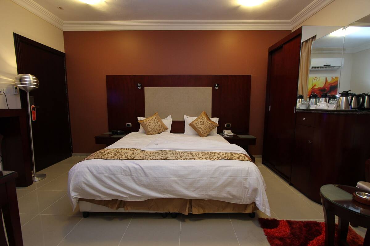 A hotel room with a large bed, a nightstand, a bedside table, a wardrobe, and a mirror.