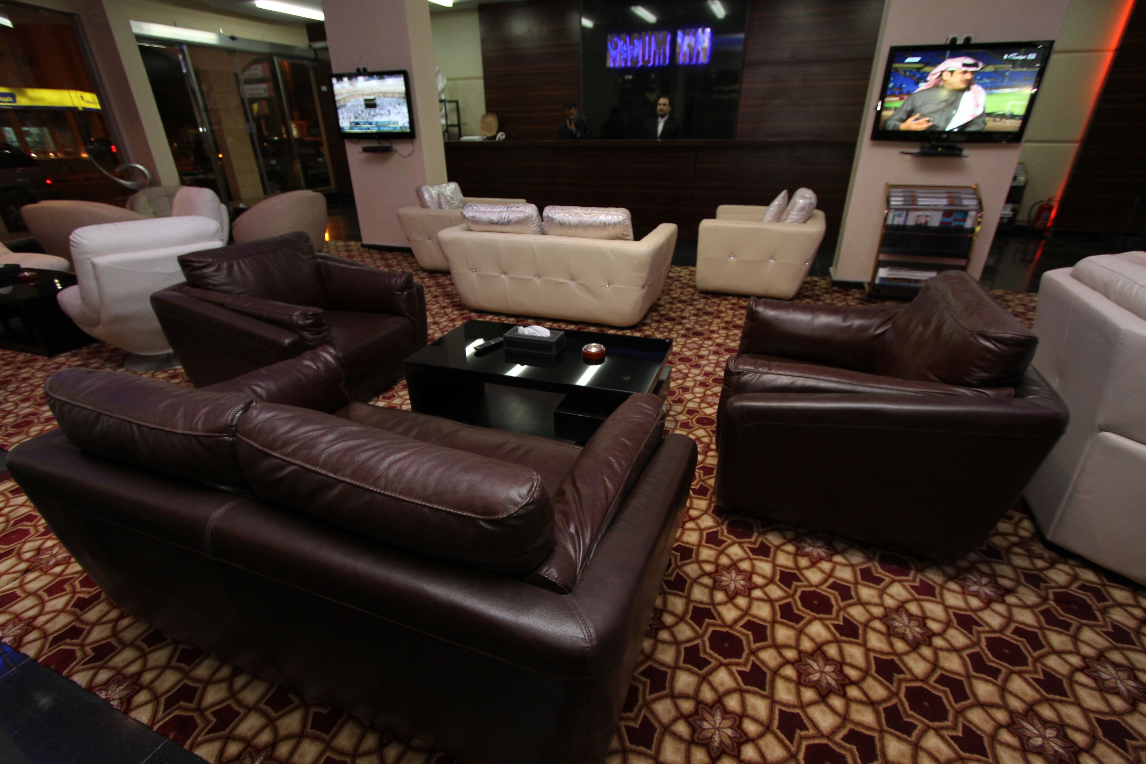 A hotel lobby with leather sofas, a coffee table, and a TV screen.
