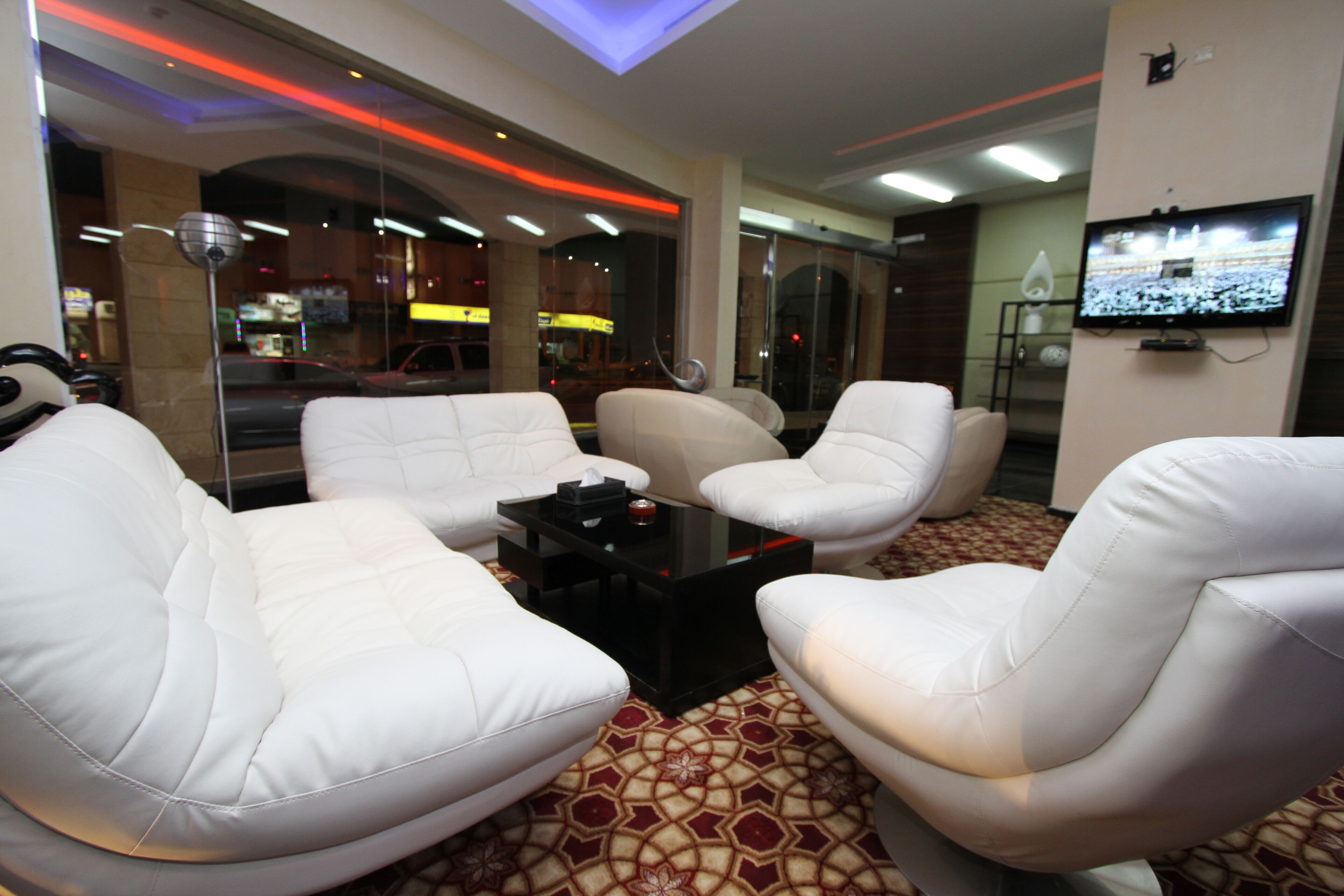 Una habitación de hotel moderna con sofás de cuero blanco, una mesa de centro negra y un televisor montado en la pared.