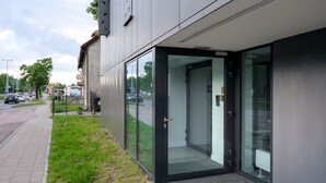 A modern building entrance with a glass door and a small grassy area beside it.