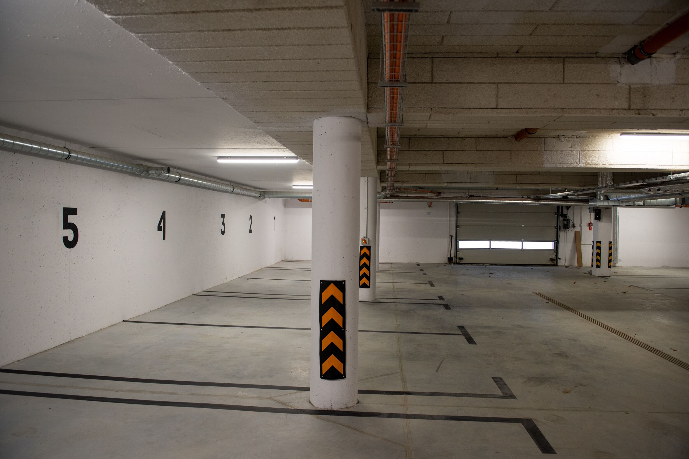 An indoor parking garage with white walls, numbered parking spaces, and safety bollards.