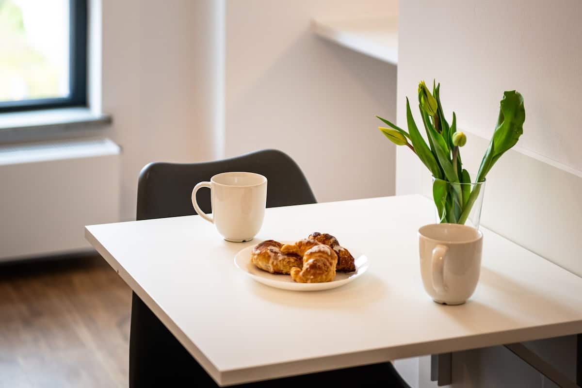 Una mesa con un plato de pasteles, una taza y un florero con flores.