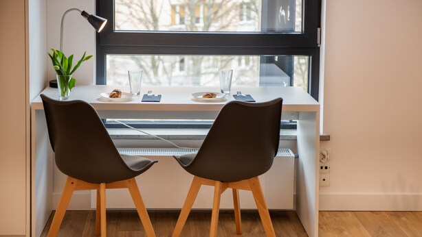 A modern workspace with two chairs, a desk, a plant, and a window with a view of buildings.