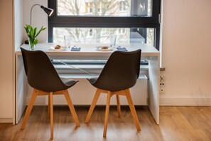 A modern workspace with two chairs, a desk, a plant, and a window with a view of buildings. - Apartamenty Olimpijskie (Gdansk)