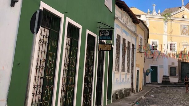 Una calle adoquinada con un edificio verde con contraventanas blancas y un letrero que dice 'Pousada'.