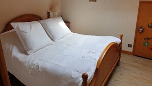 A neatly made bed with a wooden headboard, a bedside lamp, and a small decorative item on the wall. - Apartment in the Megeve valley (Praz-sur-Arly)