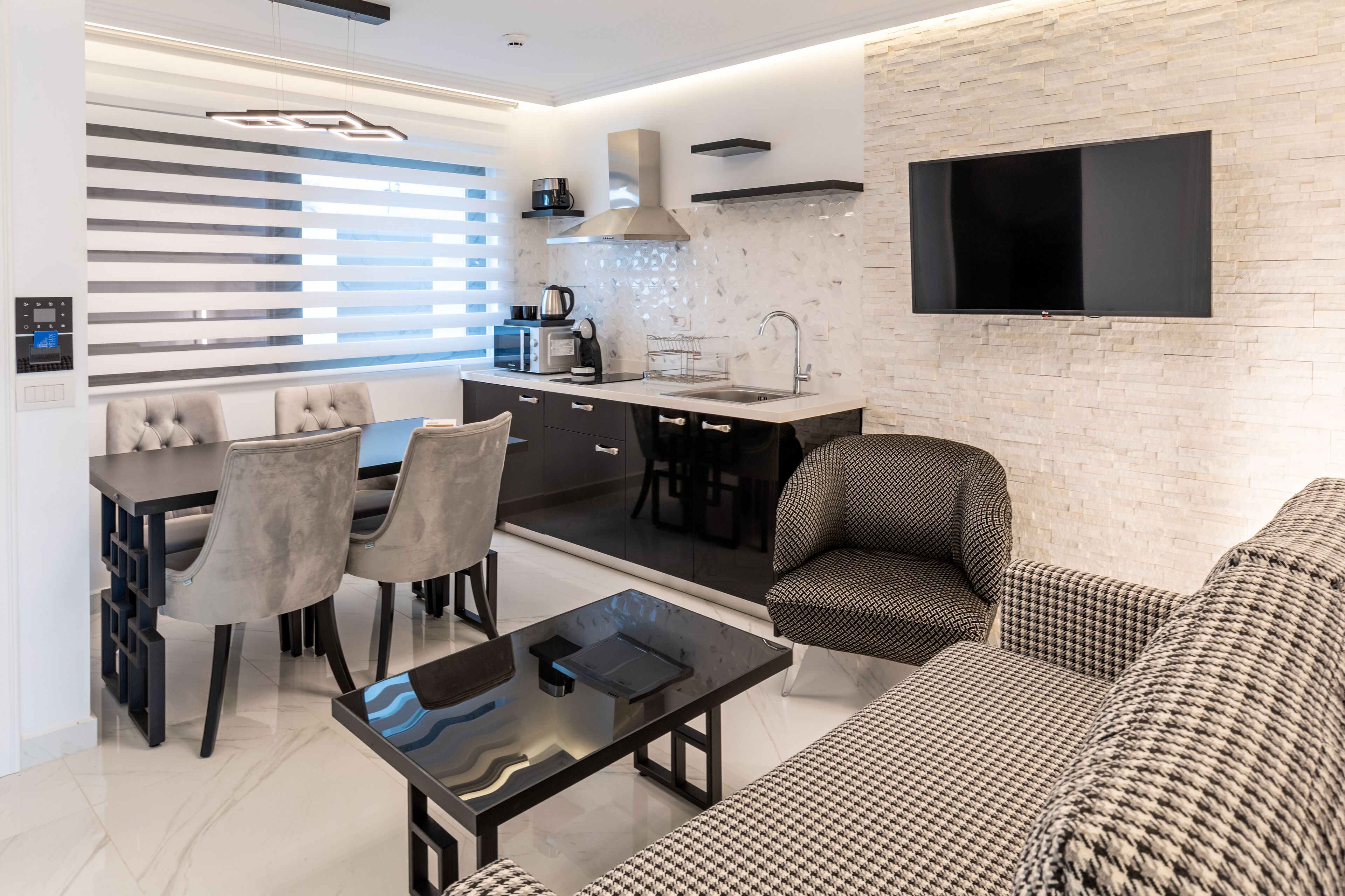 A modern kitchen with a dining area, a sofa, and a TV mounted on the wall.