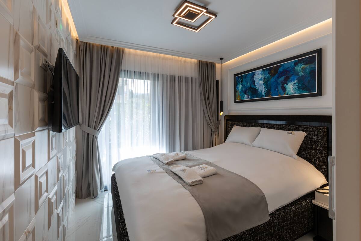 Une chambre d’hôtel moderne avec un grand lit, un téléviseur à écran plat fixé au mur et un tableau au-dessus du lit.