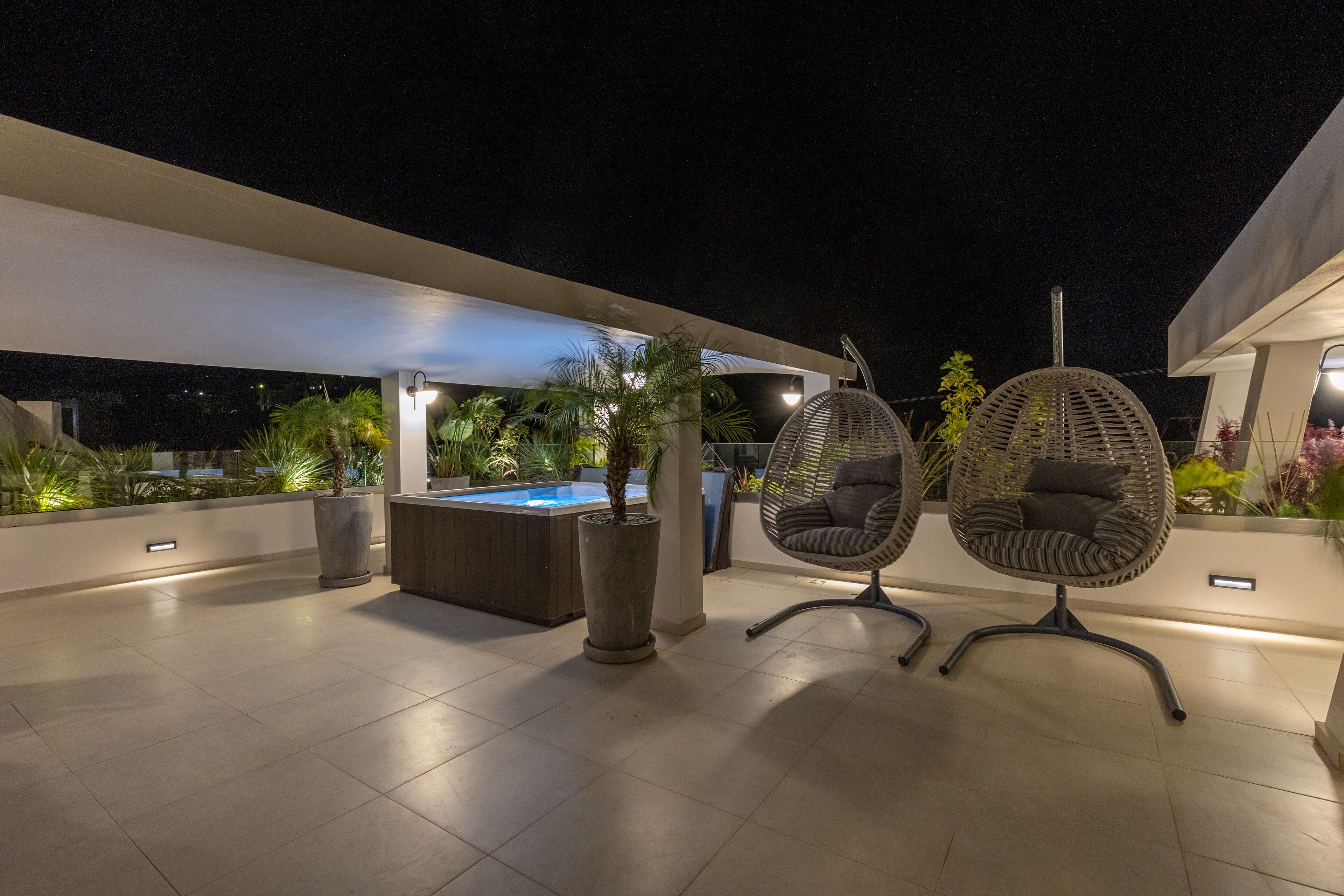 An outdoor terrace with a hot tub, two wicker chairs, and potted plants.