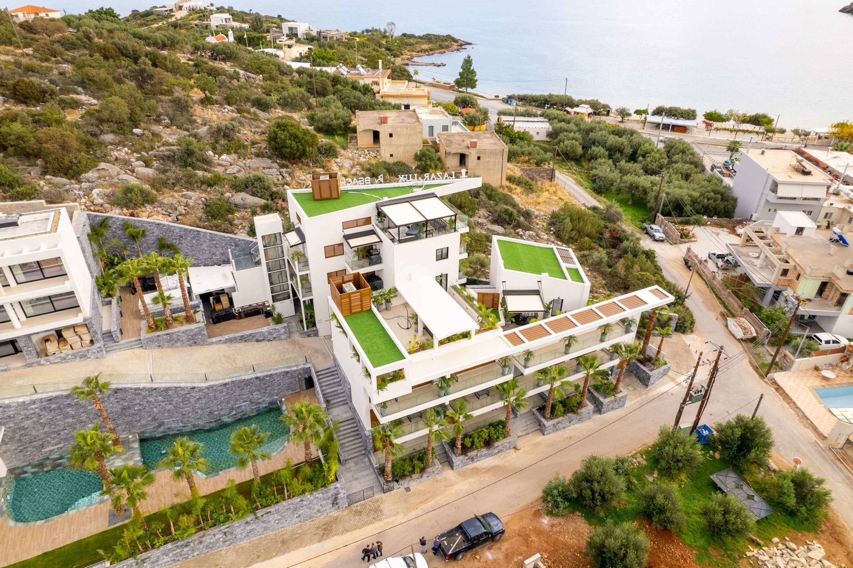 Un immeuble moderne à plusieurs étages, doté d’une piscine sur le toit, entouré de verdure et offrant une vue sur la côte.