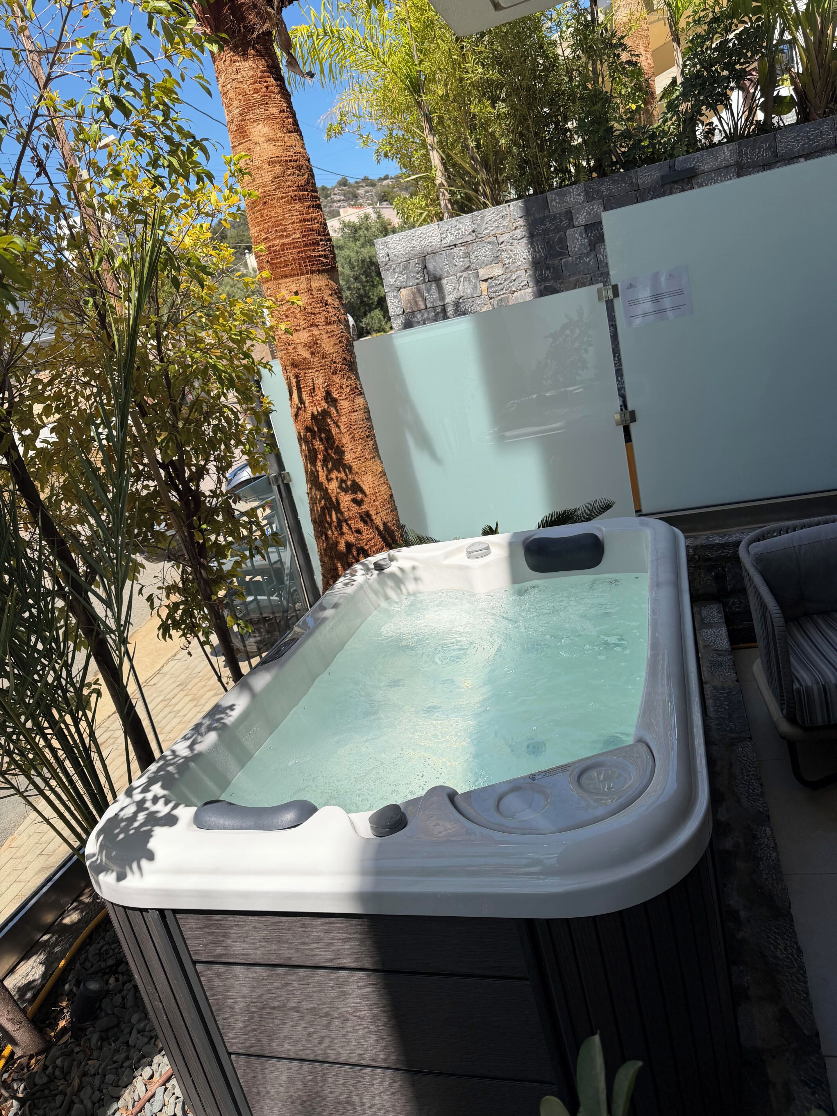 Un bain à remous installé à l’extérieur, avec un mur en pierre, un arbre et une chaise.