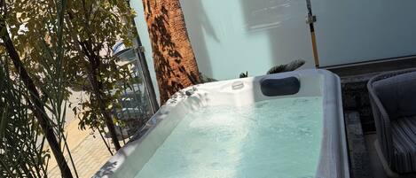 A hot tub in an outdoor setting with a stone wall, a tree, and a chair.