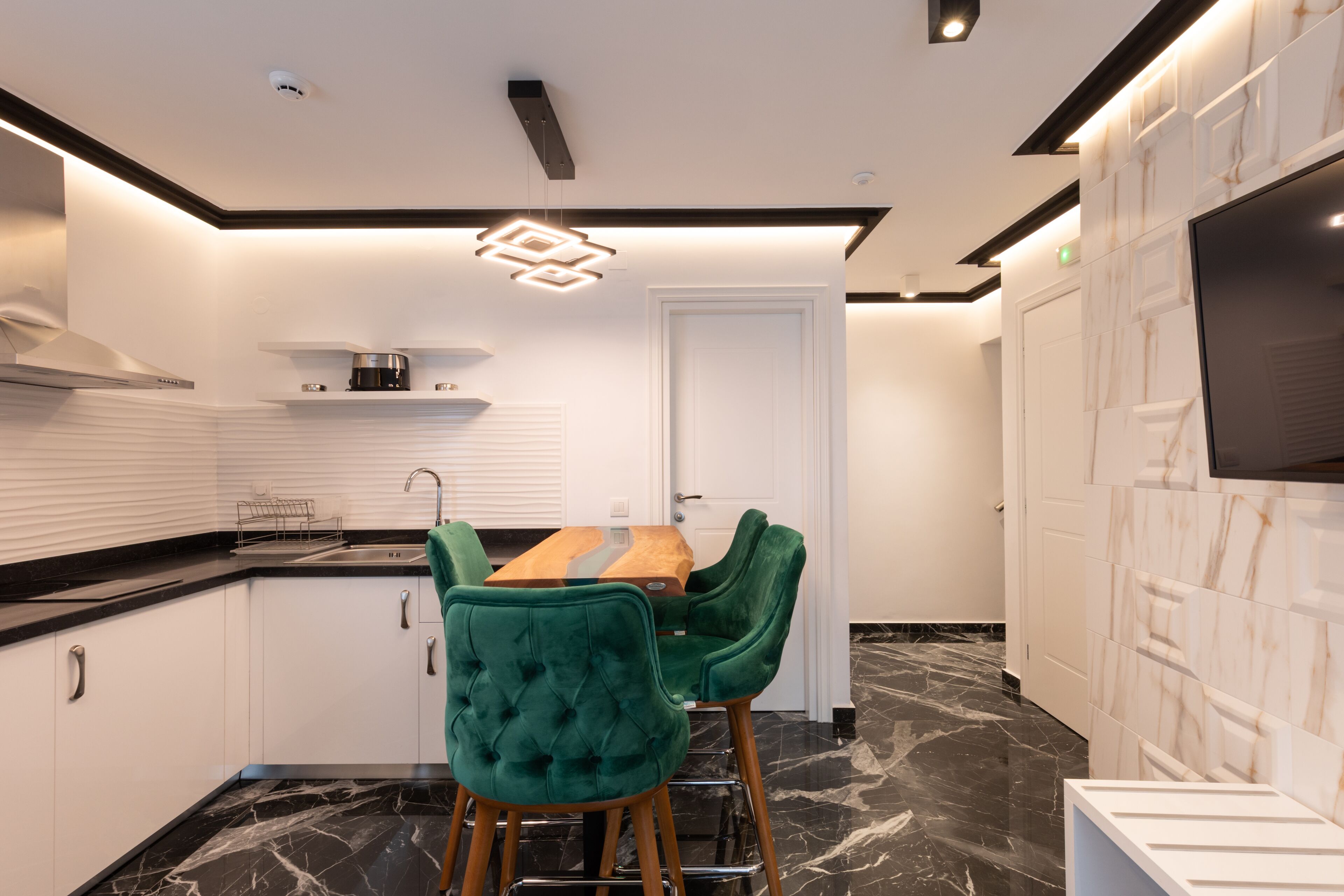 Une cuisine moderne avec des meubles blancs, un plan de travail en marbre et une table à manger en bois, assortie de chaises à revêtement vert.