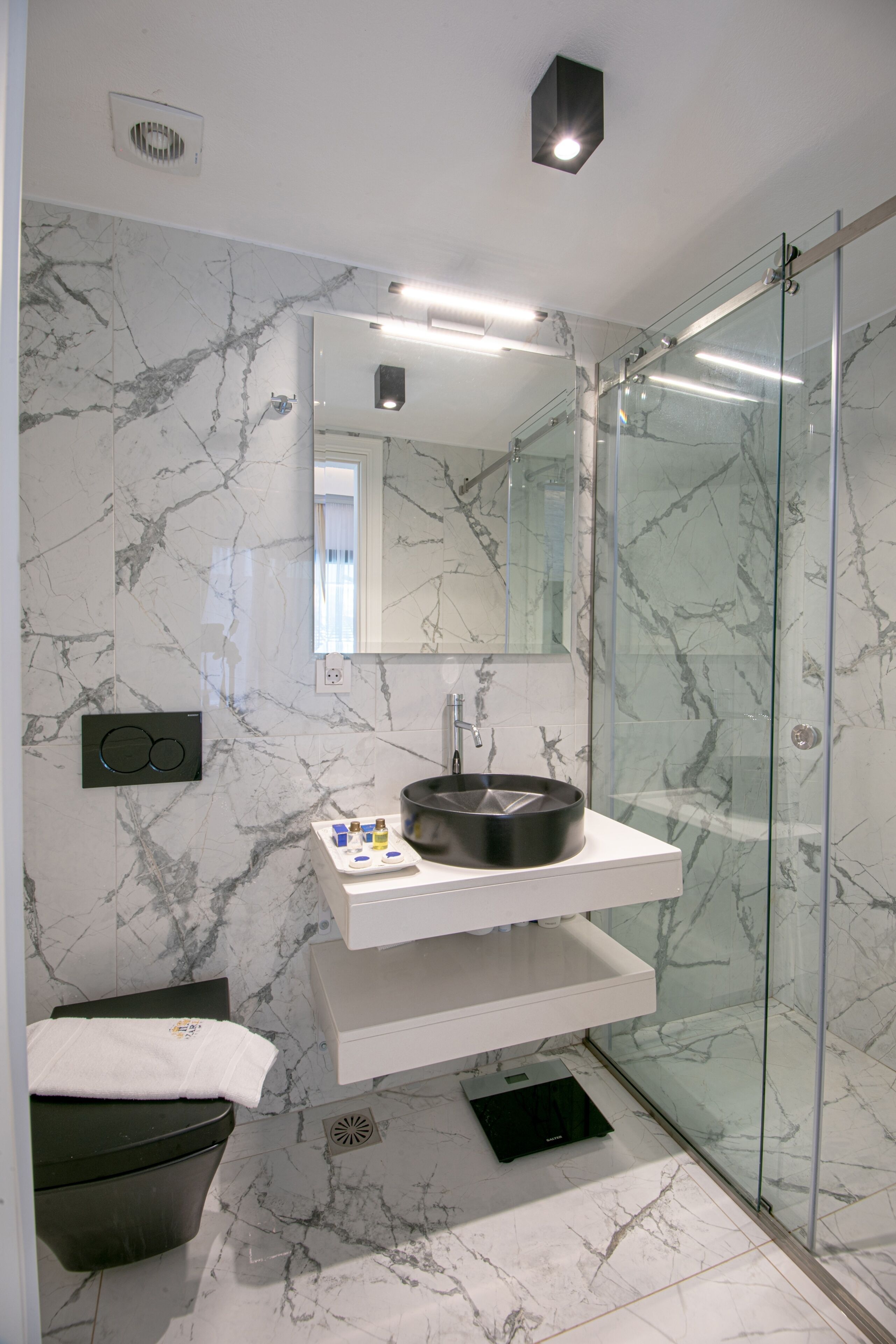 Un baño moderno con salpicadero de mármol, cabina de ducha con mampara de cristal y lavamanos negro.