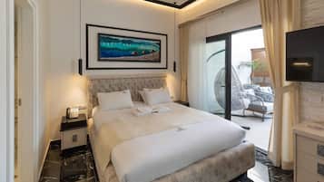 A modern hotel room with a large bed, a flat-screen TV, a painting above the bed, and a balcony with outdoor seating.