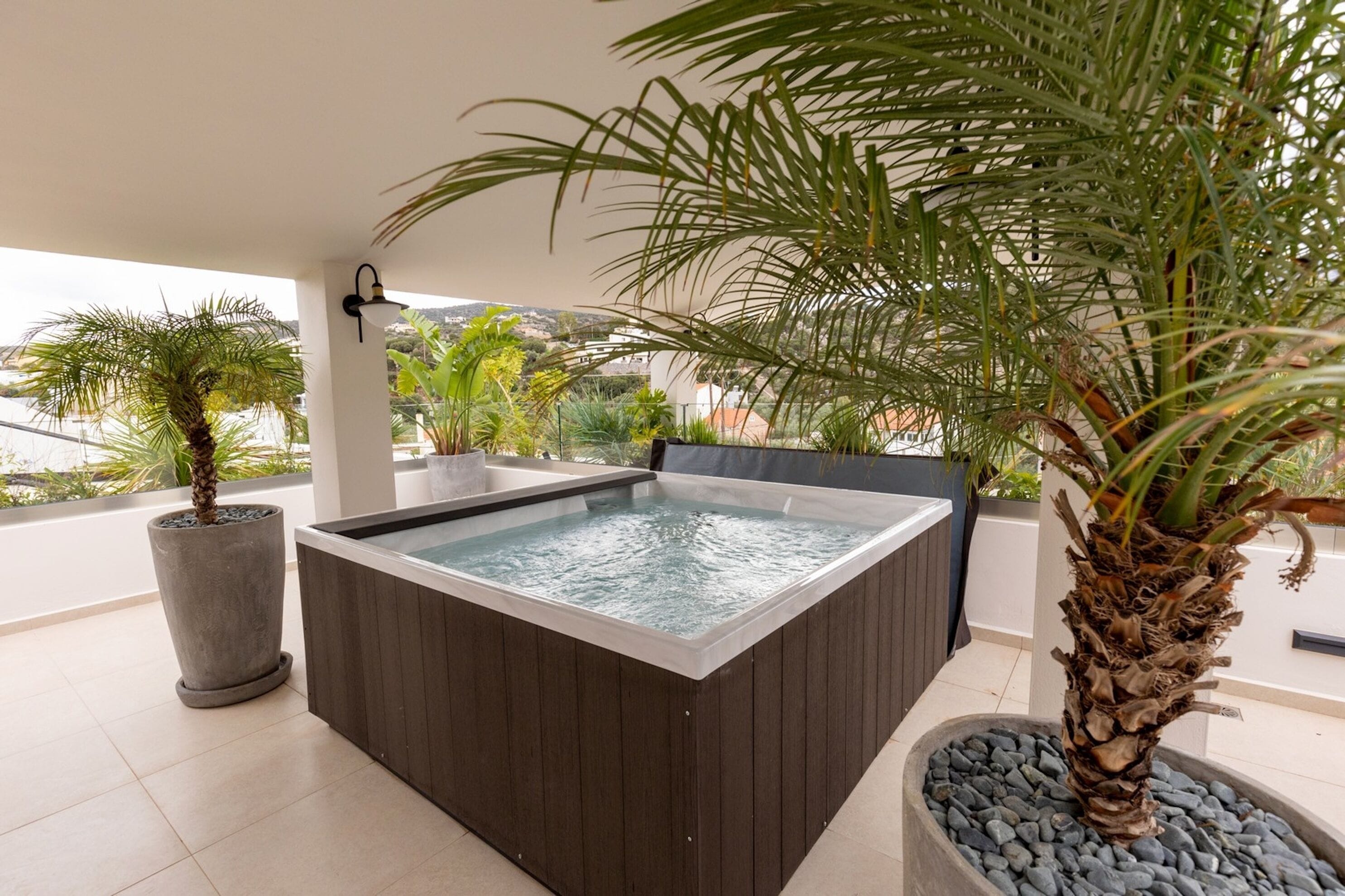 A hot tub on a balcony with surrounding plants and a view of the landscape.