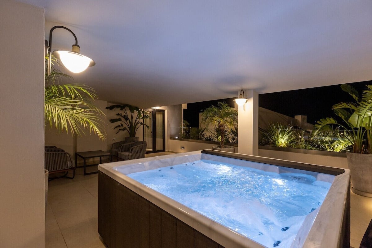 Un bain à remous avec vue sur le ciel nocturne, entouré de plantes en pot et agrémenté d’un espace salon.