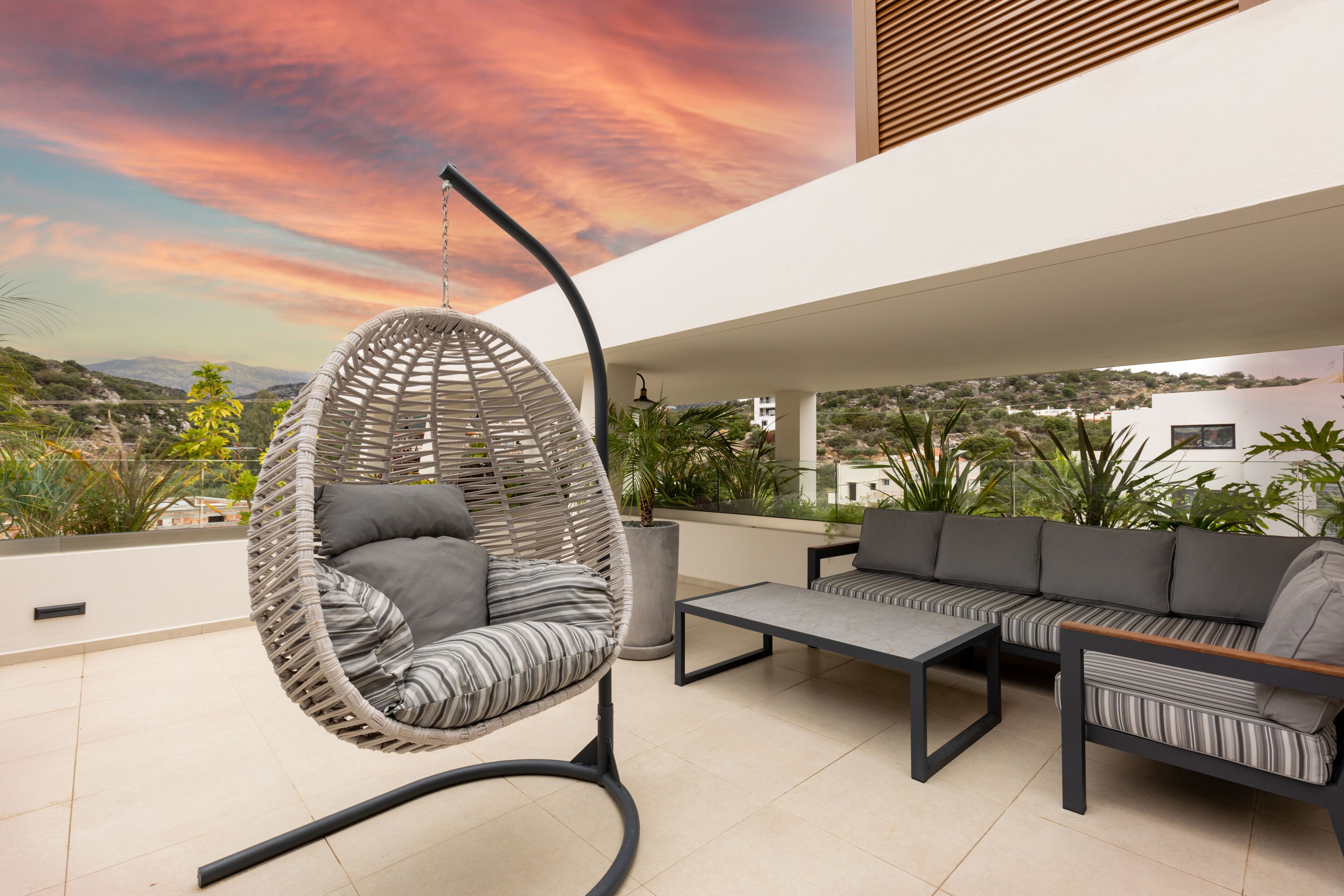 A modern outdoor seating area with a hanging chair, a sofa, and a coffee table.