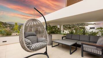 A modern outdoor seating area with a hanging chair, a sofa, and a coffee table.