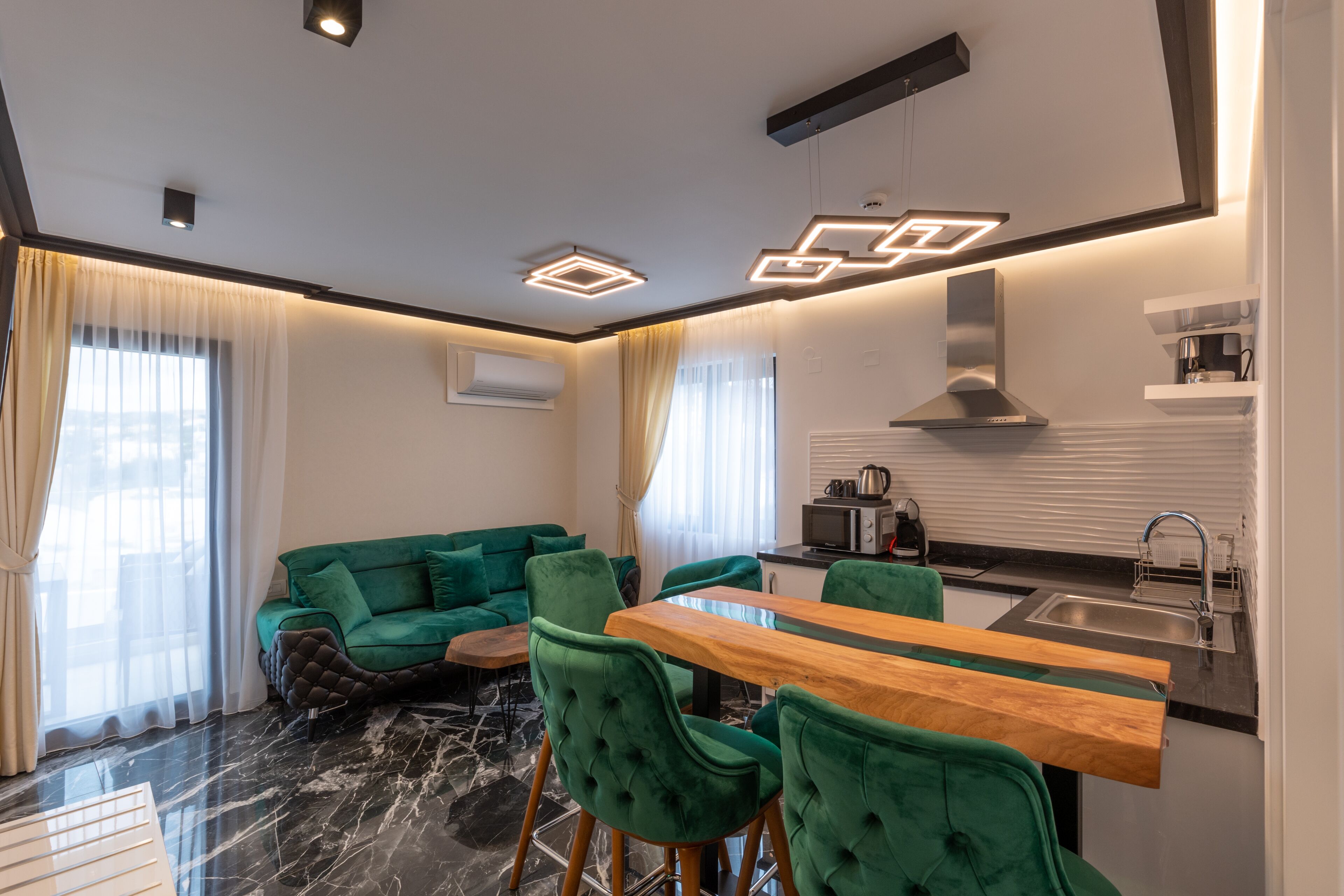 A modern living room with a green sofa, a wooden dining table, and a kitchen area with a sink and stove.