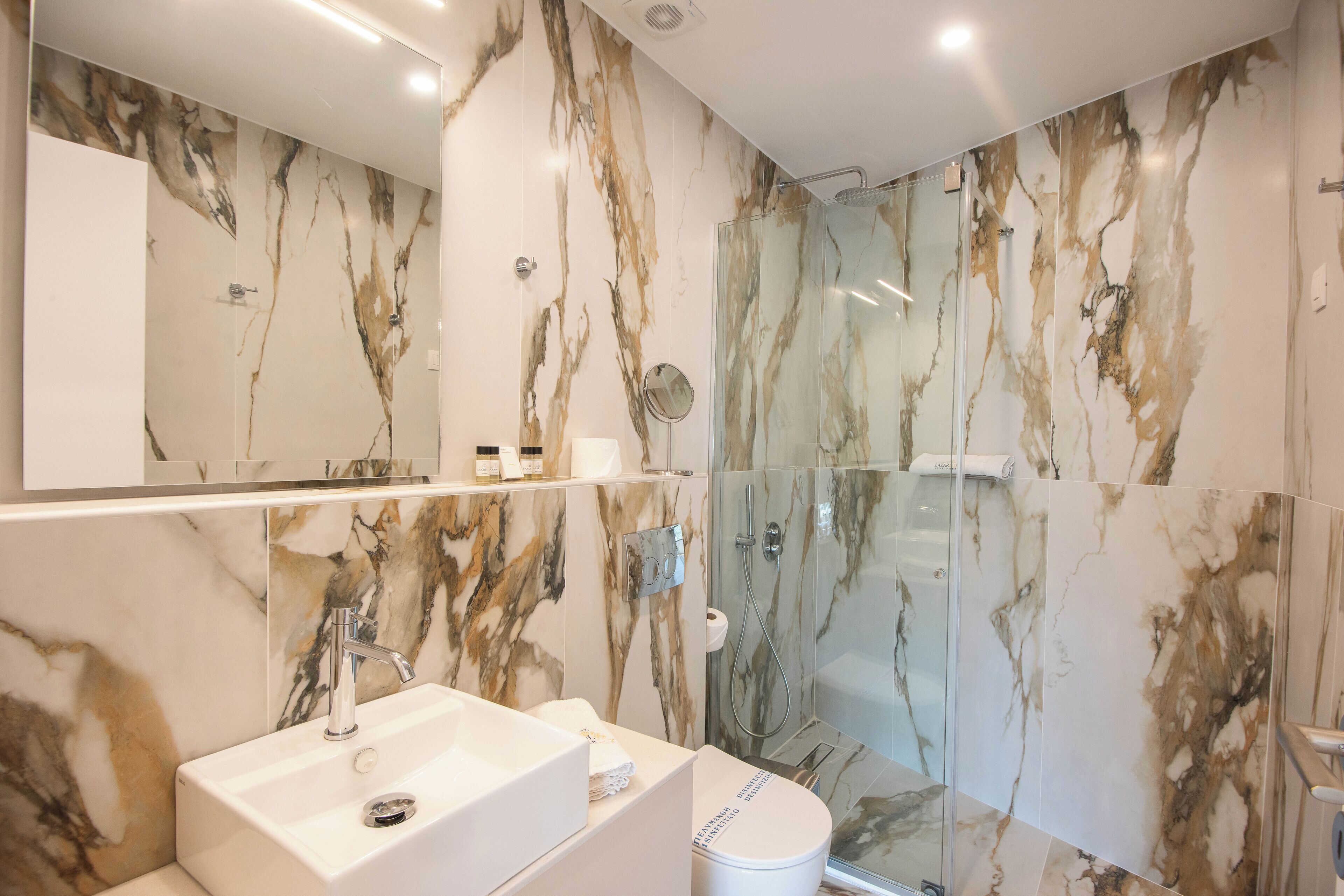 Un baño moderno con salpicadero de mármol, ducha con cerramiento de vidrio y lavamanos blanco.