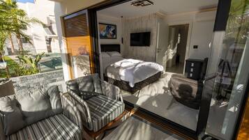 Un dormitorio moderno con cama, televisor y puerta de vidrio que da a un balcón con sofá y sillón.