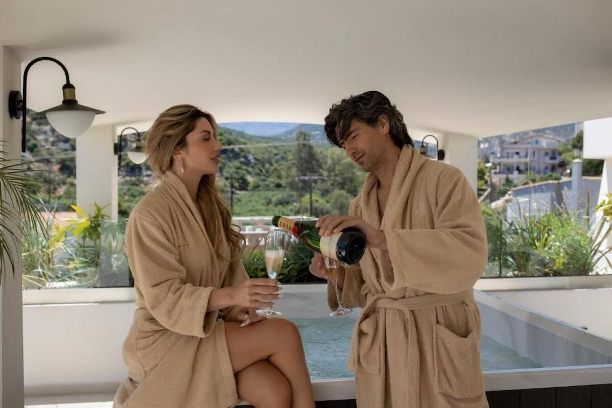 Un couple, vêtu de peignoirs, est assis au bord d’une piscine, avec une vue sur les montagnes.