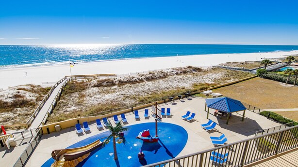 A beachside resort with a pool area, lounge chairs, and a lifeguard stand.