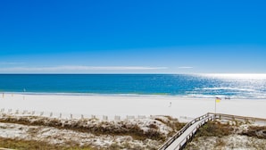 A beach with a wooden boardwalk leading to the water, a sandy shore, and a clear blue sky.