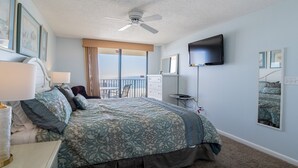 A hotel room with a bed, a TV, a balcony with a view, and a ceiling fan.