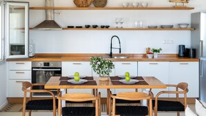 Une cuisine moderne avec des armoires blanches, des comptoirs en bois et un îlot central doté de chaises. Des étagères au-dessus du comptoir servent à ranger des bols et des verres.