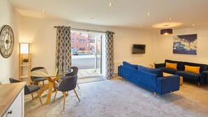 A modern living room with a glass table, blue sofa, and a TV mounted on the wall. - Host & Stay | West Cliff Retreat (Whitby)
