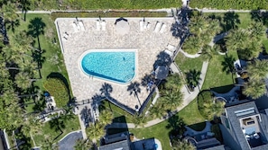 Vista aérea de un resort con piscina, palmeras y un camino pavimentado.