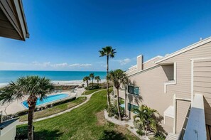 A beachfront hotel with a swimming pool, palm trees, and a clear view of the ocean.