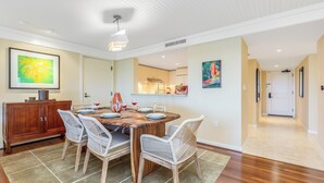 Un coin repas avec une table en bois, des chaises en osier et un tapis. On y trouve également un buffet sur lequel sont posés un vase et des verres à vin.