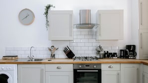 Een moderne keuken met witte kastjes, een roestvrijstalen afzuigkap, een inbouwoven en een koffiezetapparaat.