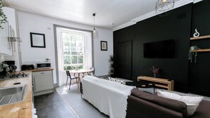 Een moderne keuken met een eethoek, een woonkamer met een bank en een tv aan de muur.