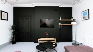 Een moderne woonkamer met een zwarte accentmuur, een flatscreen televisie bevestigd boven een houten console en een potplant.