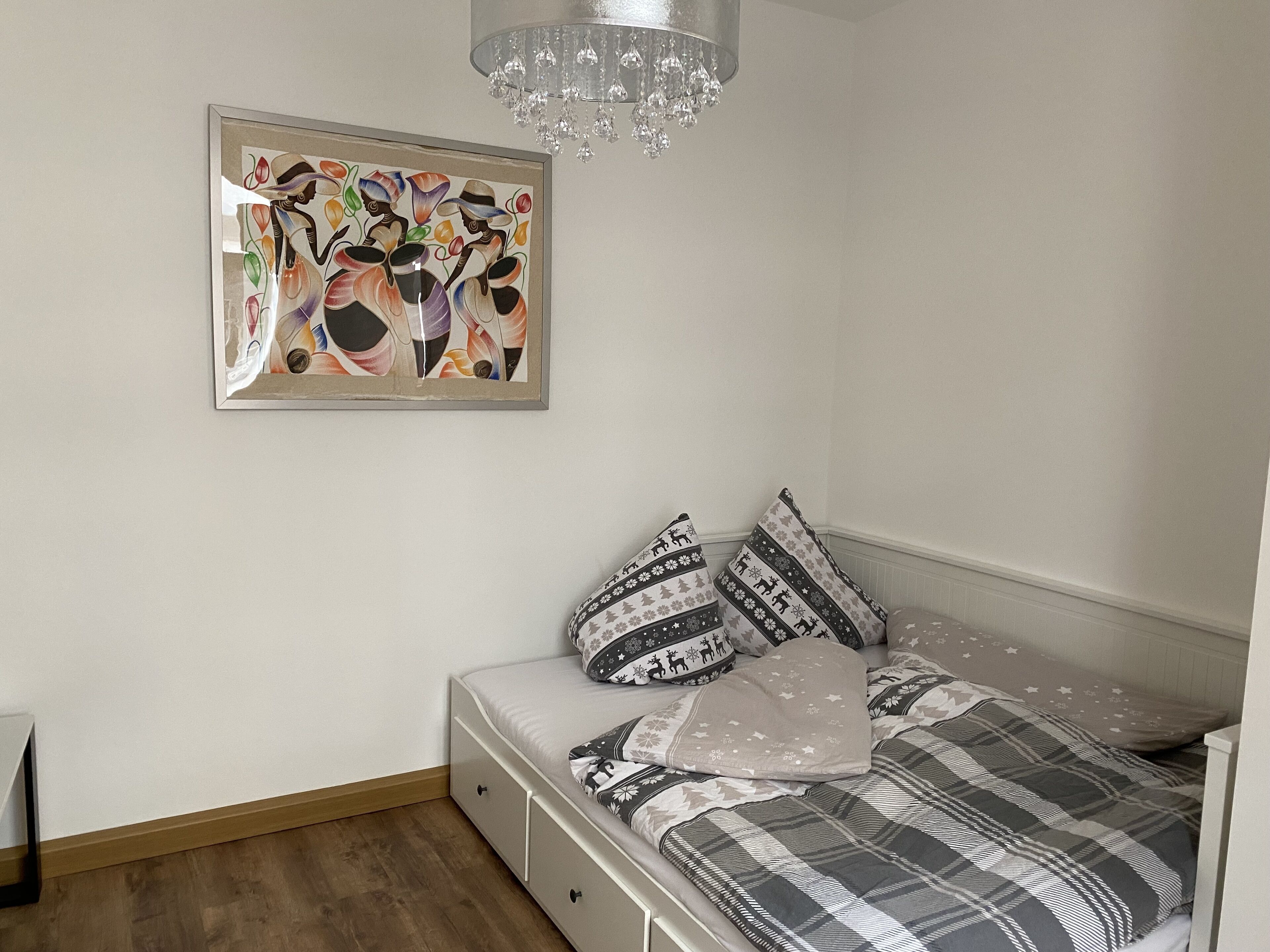 A bedroom with a bed, pillows, a dresser, a framed artwork, and a chandelier.
