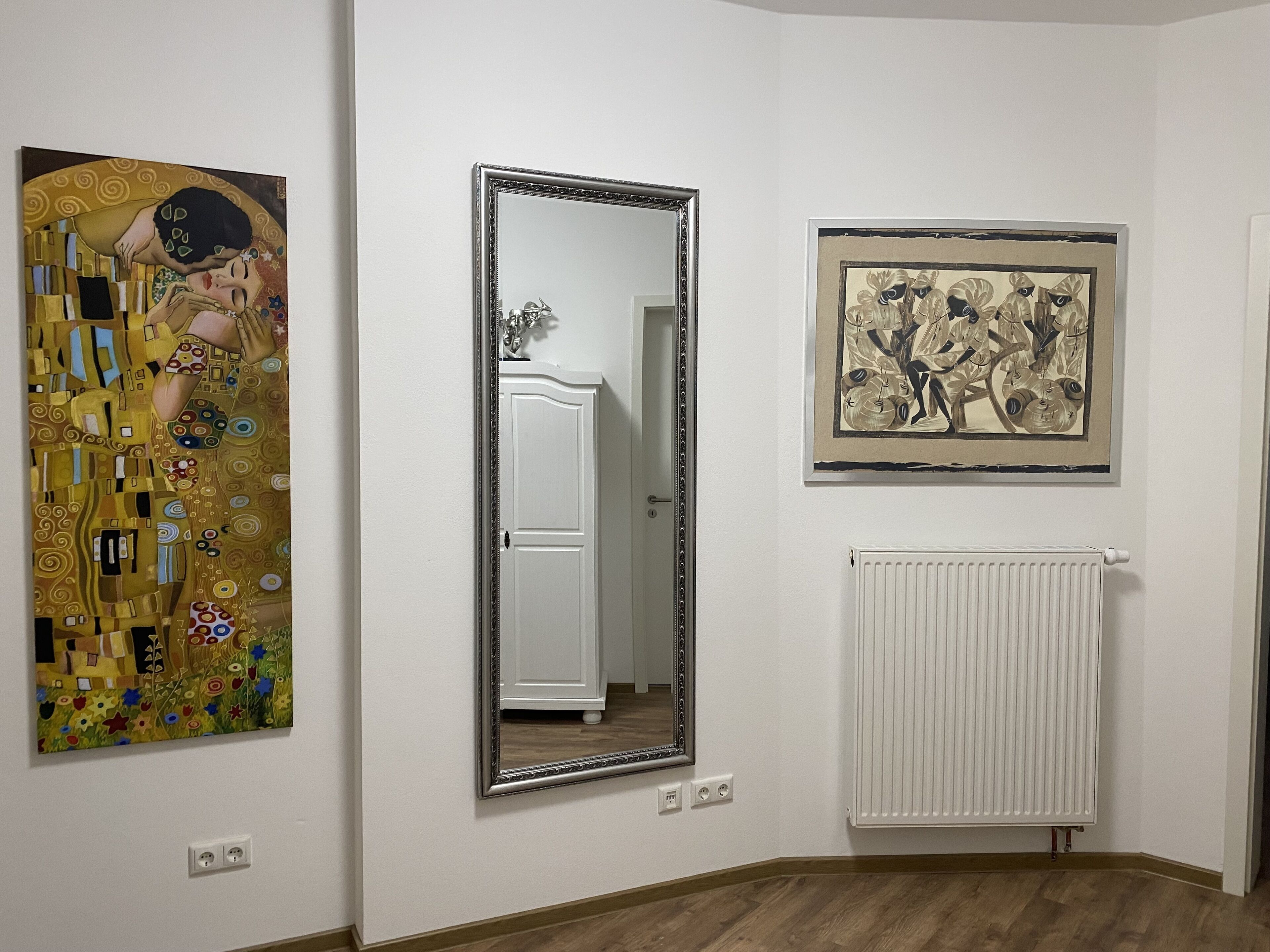 A room with a large mirror, a radiator, and two framed artworks on the wall.