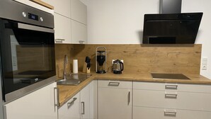 Moderni keittiö, jossa on valkoiset kaapit, ruostumattomasta teräksestä valmistettu uuni, kahvinkeitin ja mikroaaltouuni.