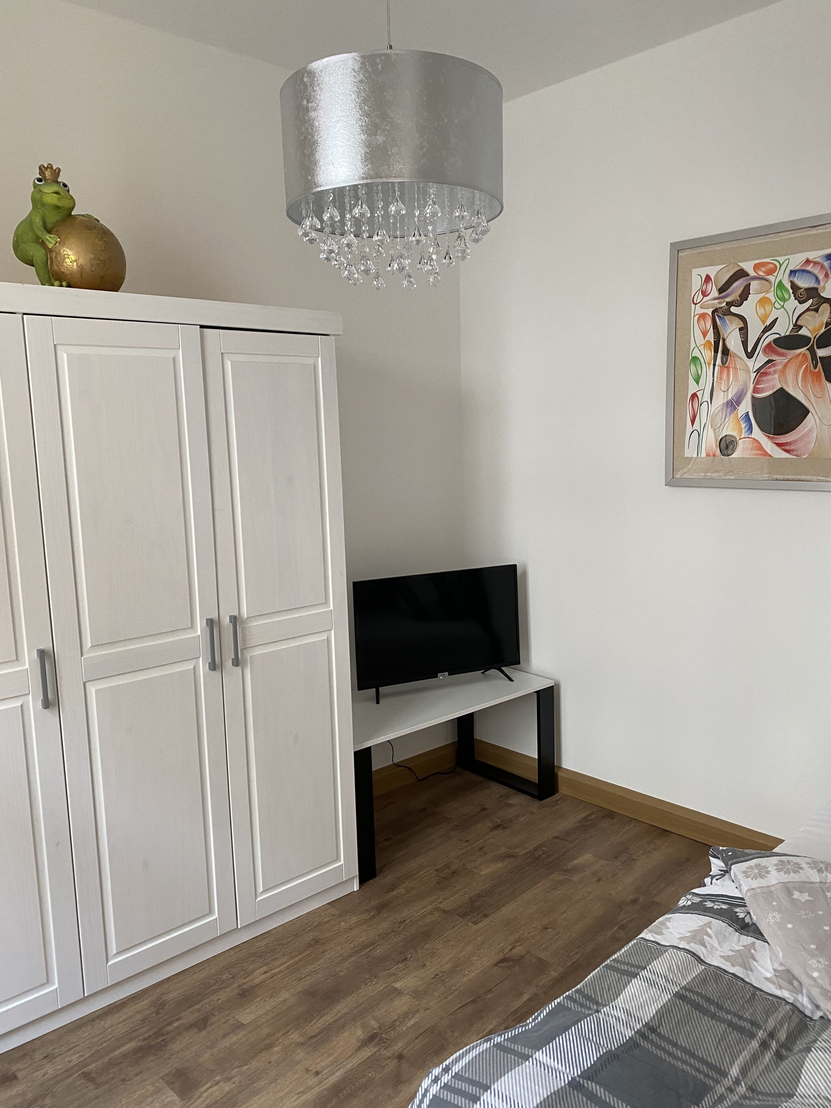 A bedroom with a wardrobe, a television on a stand, a bed, and a chandelier.