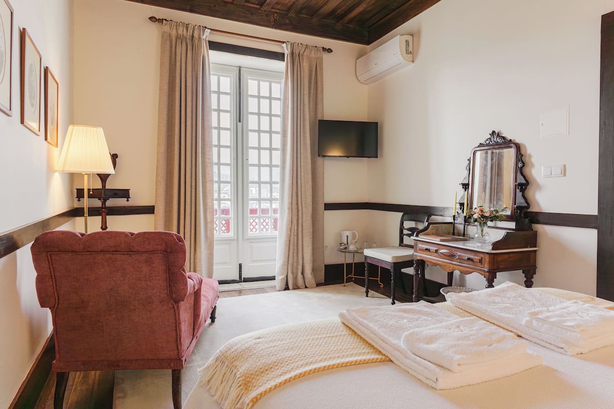 Quarto de hotel com cama, escrivaninha, cadeira, televisão e janela com cortinas.