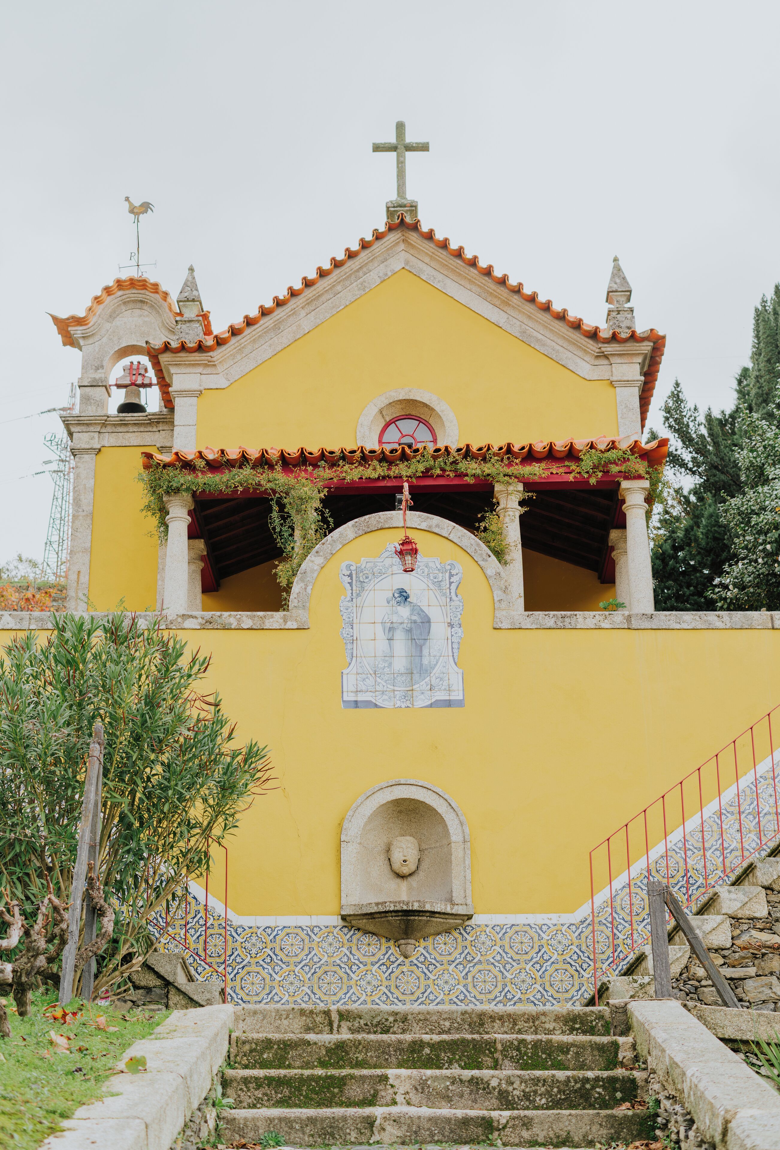 A yellow church with a bell tower, a cross, and a tiled entrance.