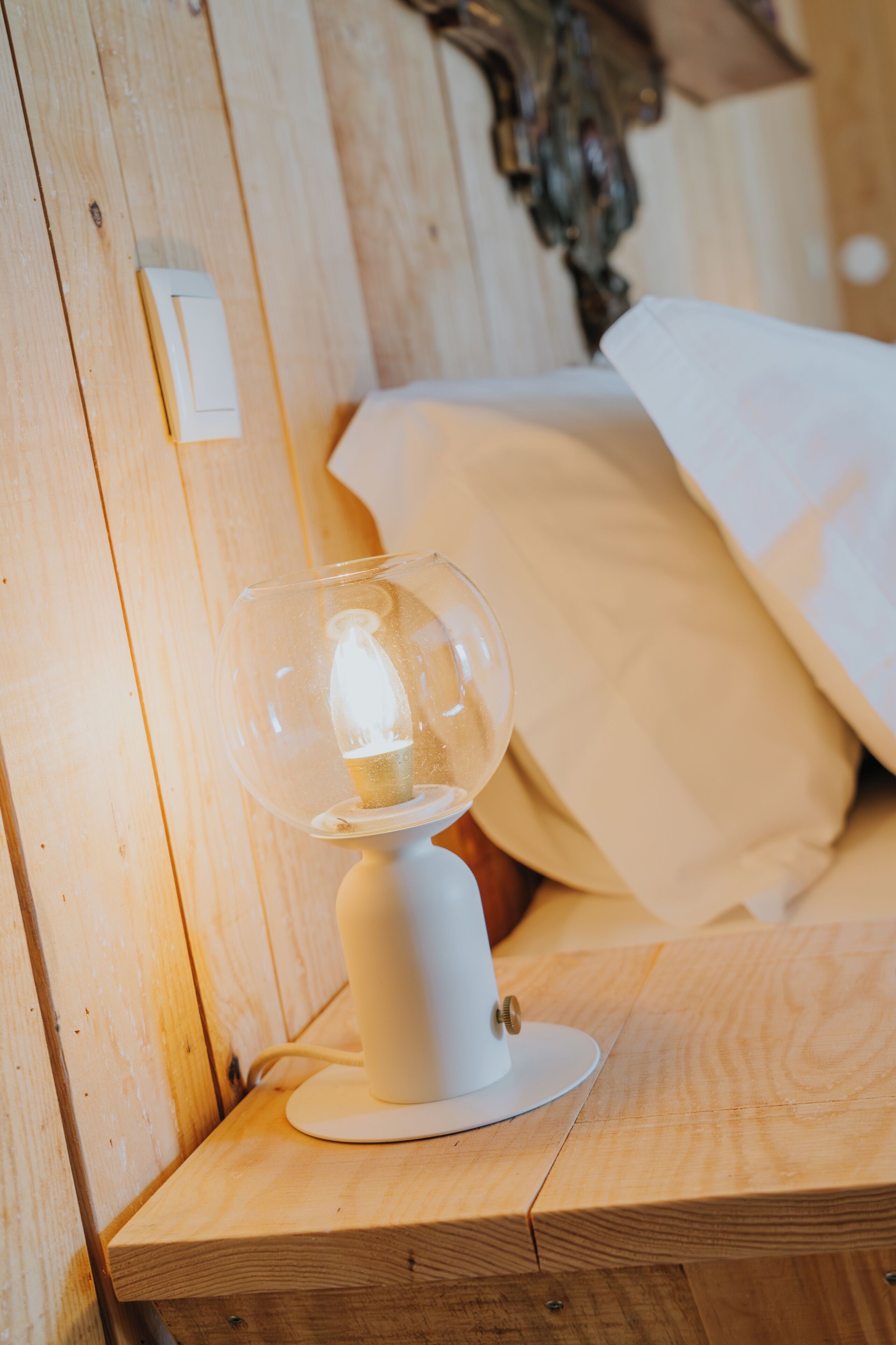 A wooden bedside table with a white lamp and a white bedspread.