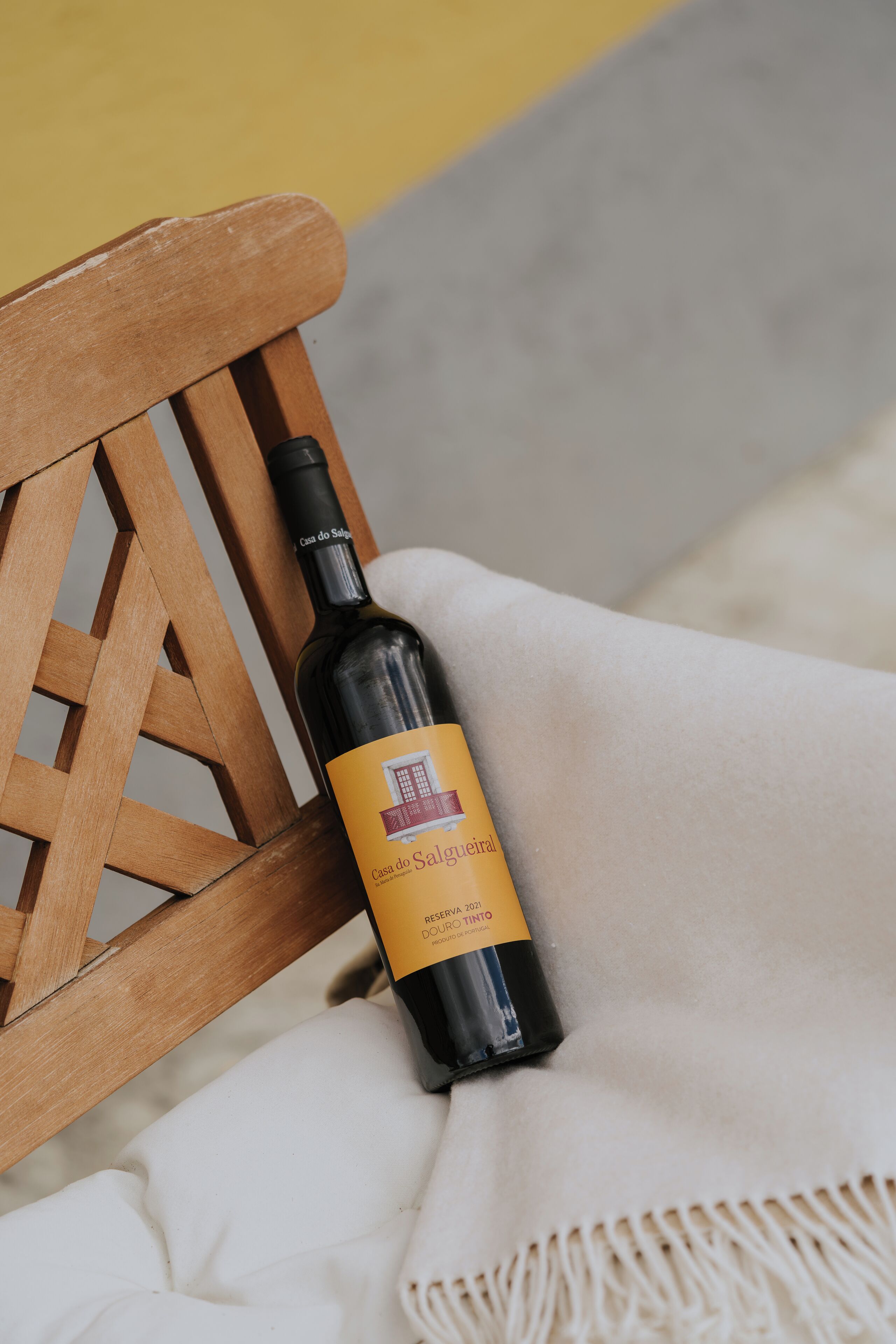 A bottle of wine on a white cloth next to a wooden chair.